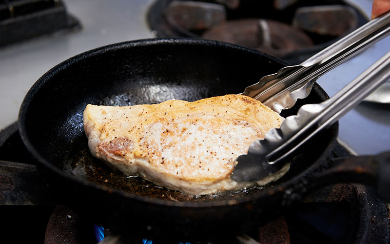 フライパンで焼き目をつけている豚料理