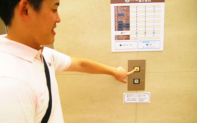 エレベーターの「昇」ボタンを押すMさん