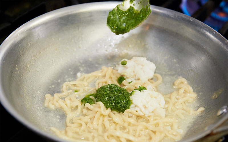 手打ちパスタとハモが入ったフライパンにバジルソースを入れる様子