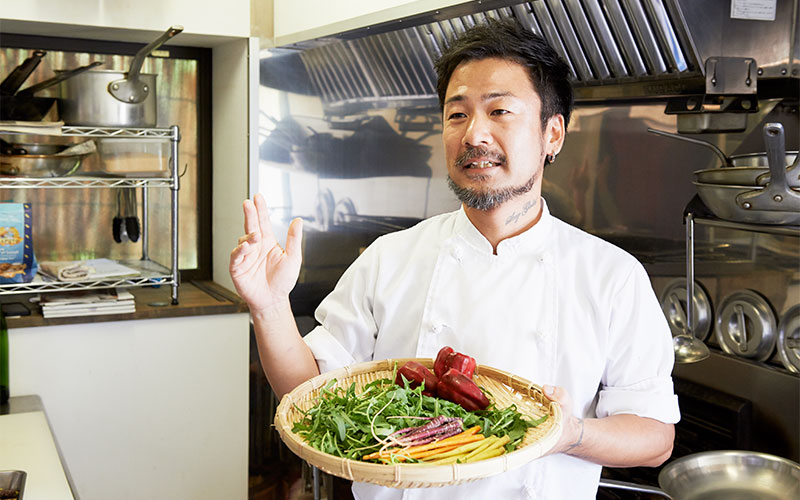 材料の野菜を手に、淡路の野菜について説明するシェフ