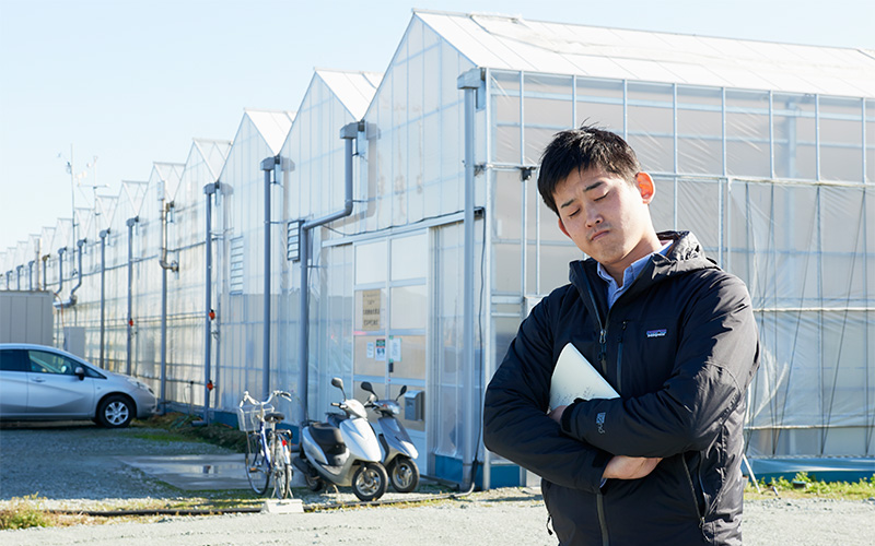 トンガリ屋根のハウスの前で首をかしげるMさん