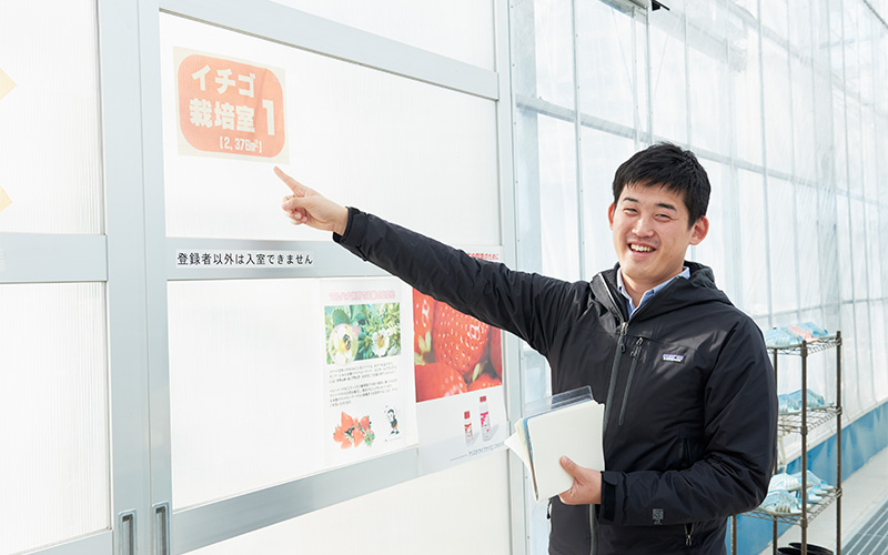 イチゴ栽培室の扉を指差す取材班Mさん