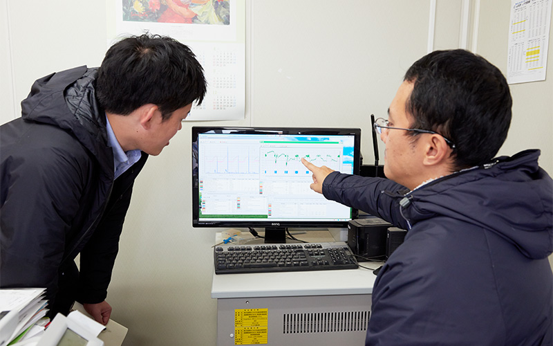 コンピューターの管理画面の説明をする上田さんと覗き込む取材班Mさん