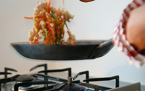 野菜を入れたフライパンを振って炒めている様子
